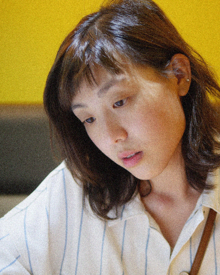 Indoor portrait, before: a woman in a striped shirt looking down, with colored speckles on her cheek and hair
